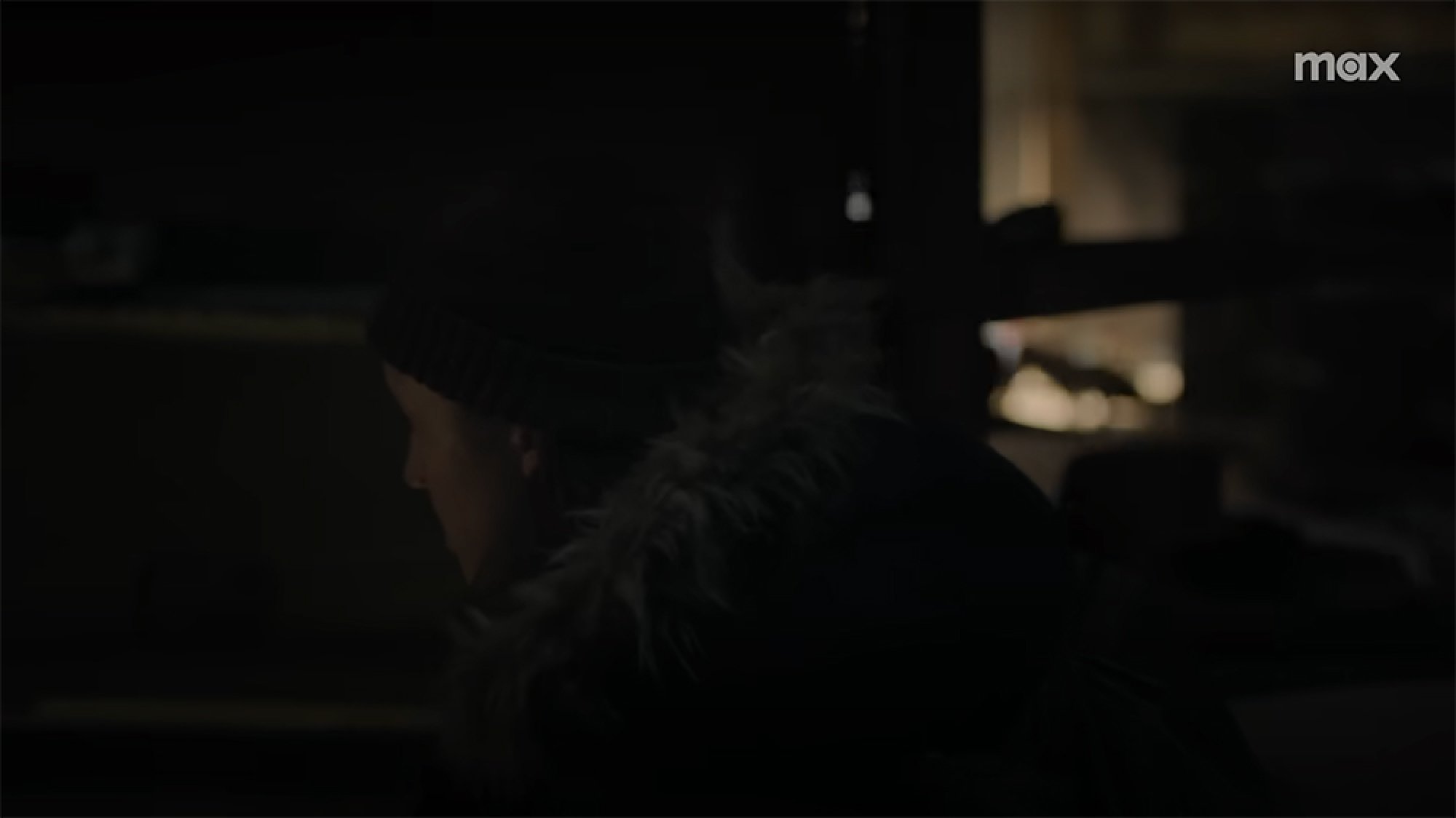 A woman hides in a dark room. Something is visible in the background.