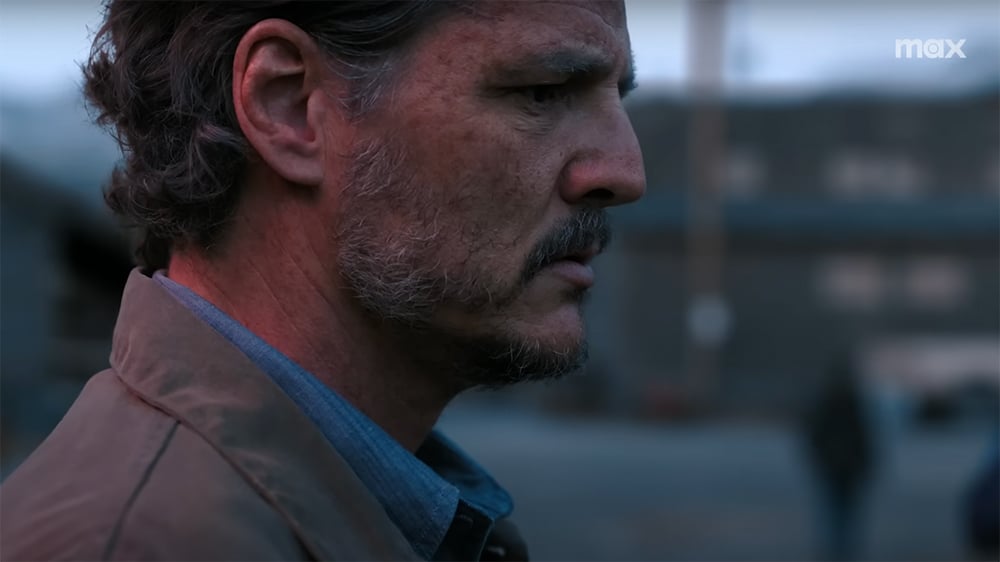 A close-up of a man's face as a person walks away in the background.