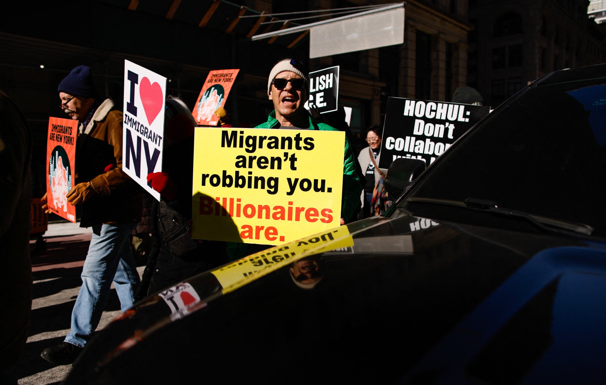A protester holds a sign that reads "Migrants aren't robbing you. Billionaires are."