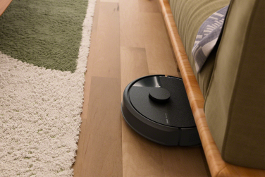 Black Roomba 105 robot vacuum cleaning under couch